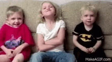 three children are sitting on a couch and one of them is wearing a batman shirt