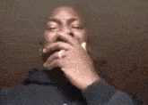 a man in a blue hoodie is smoking a cigarette with his hand on his mouth .