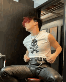 a man with red hair is sitting on a stool wearing a skull and crossbones shirt