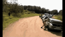 a group of people are standing on a dirt road next to cars