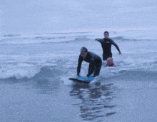 a man in a wetsuit with the letter o on his chest is helping another man on a surfboard