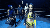 a woman in a yellow and black outfit stands in a wrestling ring with other women
