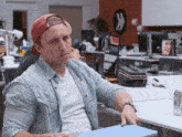 a man wearing a red hat is sitting at a desk holding a laptop