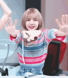 a girl in a striped sweater is sitting at a table with her hands outstretched .