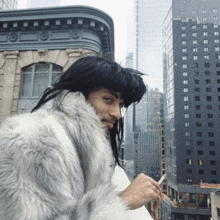 a woman in a fur coat smoking a cigarette in front of a city skyline