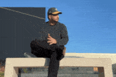 a man wearing a la hat sits on a bench with his legs crossed