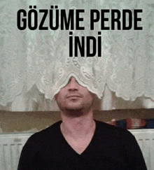 a man in a black shirt is covering his eyes with a white curtain .