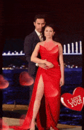 a woman in a red dress is standing next to a man in a suit with a heart that says i love you