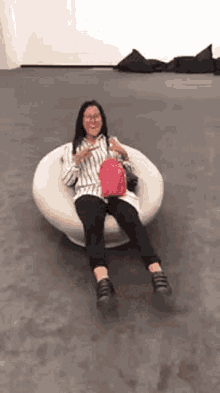 a woman is sitting in a chair with her legs crossed and a pink backpack .