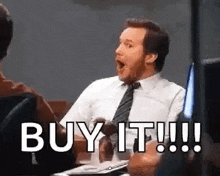 a man in a suit and tie is sitting at a table with his mouth open and saying `` buy it ! ''
