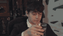 a man in a suit is drinking from a glass while sitting in a chair .