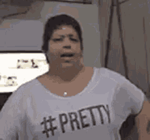 a woman wearing a white t-shirt with the word pretty on it is standing in front of a television .