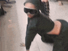 a person wearing a hoodie and goggles is kneeling down on the floor