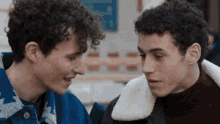 two young men with curly hair are looking at each other and smiling