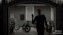 a man in a black shirt is standing in a garage with motorcycles in the background .