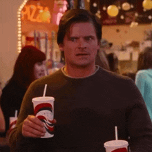 a man is holding two cups of soda in his hand .
