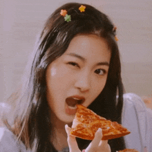 a girl with flowers in her hair is eating a slice of pepperoni pizza