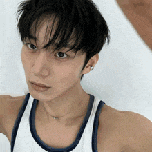 a young man wearing a white tank top and a blue necklace