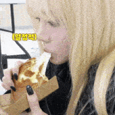 a blonde woman with black nails is eating a sandwich with a yellow sticker that says ' al '