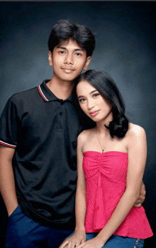 a man in a black polo shirt and a woman in a pink strapless top pose for a picture