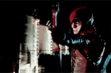 a man wearing a red jacket with a hood is standing in front of a building .