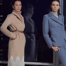 two women standing next to each other wearing suits and coats