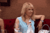 a woman in a blue shirt sits on a red couch holding a glass of water