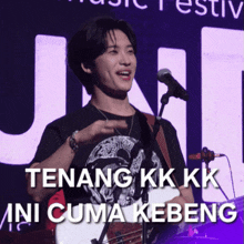 a man playing a guitar and singing into a microphone with the words tenang kk kk ini cuma kebeng above him