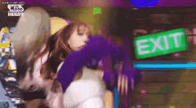 a woman in a purple sweater is dancing in front of a green exit sign