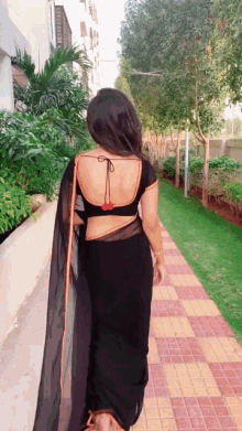 a woman in a black saree is walking down a brick path