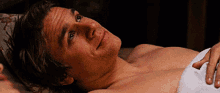 a shirtless man is laying on a bed with a white towel around his neck .