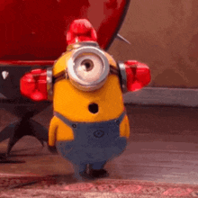 a yellow minion wearing a red hat and boxing gloves is standing on the floor .