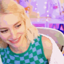 a woman in a green and blue checkered tank top is smiling while sitting in front of a computer .