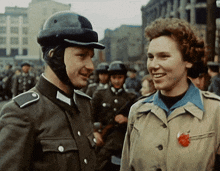 a man wearing a helmet talks to a woman in a tan jacket