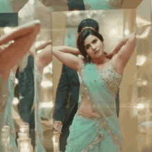 a woman in a blue and gold saree is standing in front of a mirror