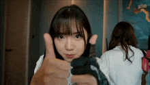 a girl giving a thumbs up with the word jkt48 on the wall behind her