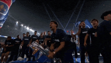 a man in a blue shirt with the word trophe on it holds a trophy