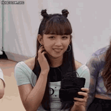 a young woman with two buns in her hair is holding a cell phone .