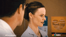 a woman in a lab coat is talking to a man in front of a sign that says " thank you "
