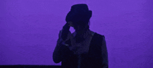 a man wearing a cowboy hat and vest is standing in front of a purple wall .