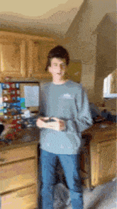 a young man is standing in a kitchen holding a remote control ..