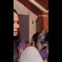 a woman in a purple shirt is sitting next to a dog in a room .