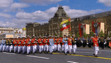 a group of soldiers marching down a street with a flag in front of them