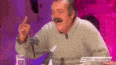 a man is laughing while sitting at a table with a glass of water and a microphone