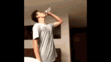 a man in a grey shirt is drinking a glass of water
