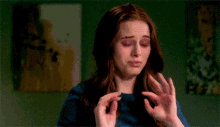 a woman with red hair and a blue shirt is making a funny face with her hands in the air .
