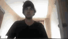 a man wearing a black hat and a black shirt is standing in a hallway .