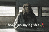 a man with long hair and glasses is sitting at a table with the words bro is jus saying shit behind him