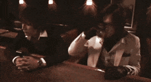 a man in a suit is sitting at a bar with his hands folded and a glass of whiskey .
