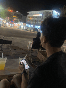a man sits at a table looking at his phone and drinking